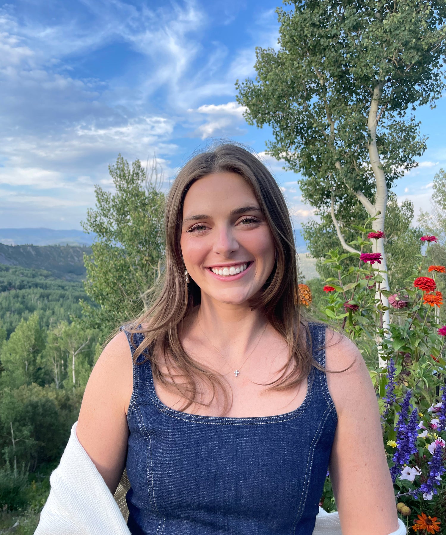 Woman in a blue dress standing outdoors with trees and flowers in the background